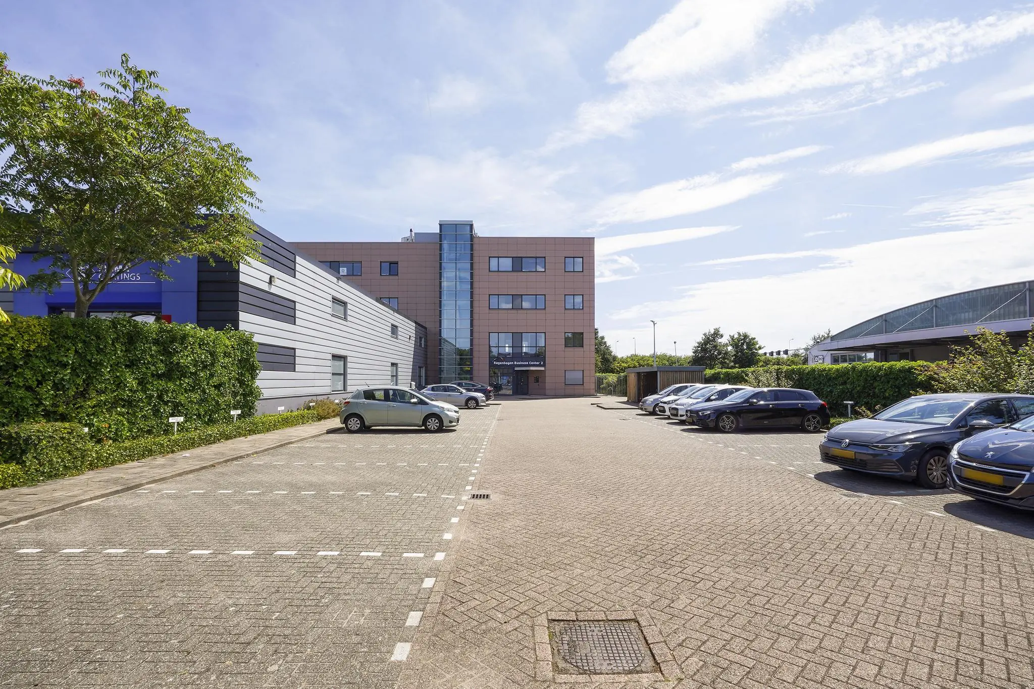 Bedrijventerrein met parkeerplaats aan de Laan van ‘s-Gravenmade, met modern kantoorgebouw en geparkeerde auto’s.